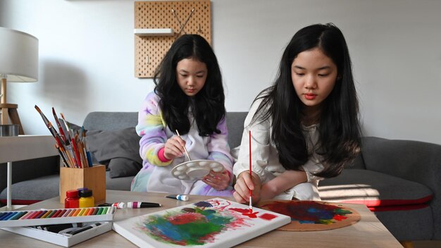 cute asian children are painting with water color together in living room