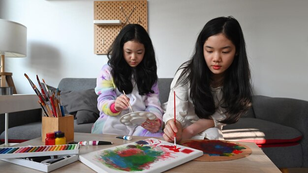 Cute asian children are painting with water color together in living room