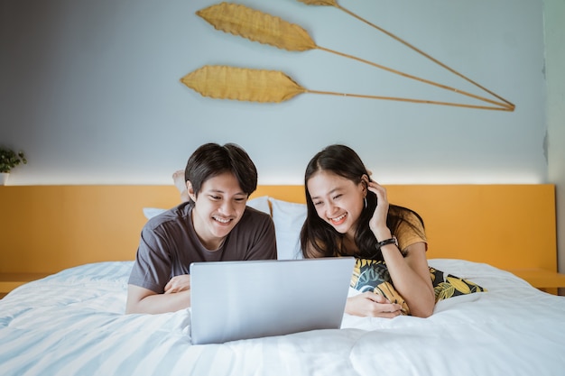 Coppie asiatiche sveglie che si rilassano insieme sul letto facendo uso del computer portatile a casa nella camera da letto