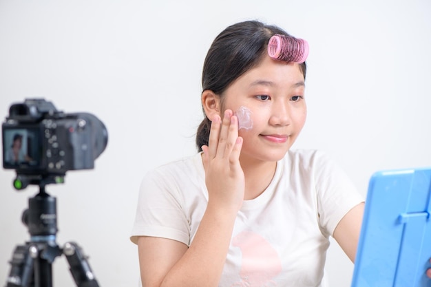 Милая азиатская блогерка наносит крем на щеки перед камерой