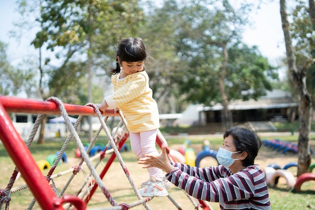 かわいいアジアの女の子と母親の笑顔が学校や幼稚園の庭や遊び場で遊ぶ