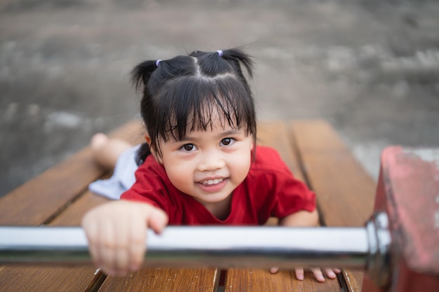 Cute asian girl play on school or kindergarten yard or playground Healthy summer activity for children Little asian girl climbing outdoors at playground Child playing on outdoor playground