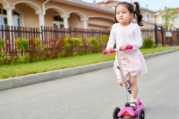 かわいいアジアの女の子のスクーターに乗って