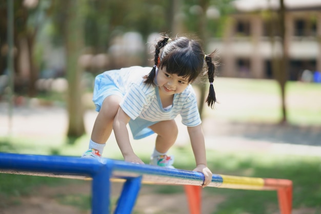 Cute asian girl smile play climb the bar on school or kindergarten yard or playground Healthy activity children Little girl climbing outdoors at playground Child playing on outdoor playground