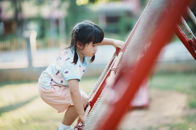 Cute asian girl smile play on school or kindergarten yard or\
playground healthy summer activity for children little asian girl\
climbing outdoors at playground child playing on outdoor\
playground