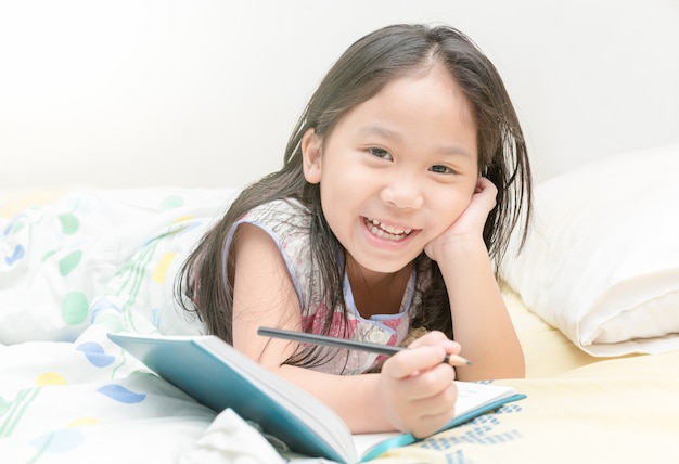 cute asian girl smile and writing to diary on the bed