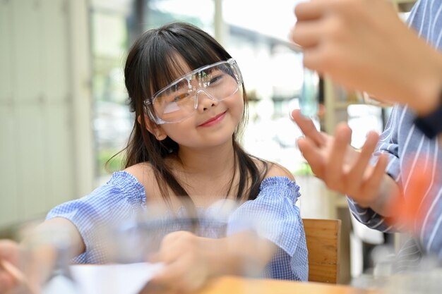 Cute asian girl with goggles enjoys learning science and doing an experiment with her teacher