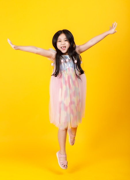 Cute Asian girl with long hair and pretty kid dress take isolated beautiful portrait on yellow background.