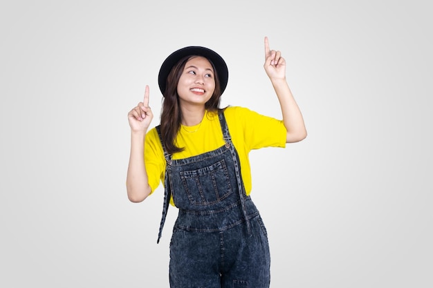 Foto ragazza asiatica sveglia in cappello giallo e nero con la mano rivolta verso l'alto