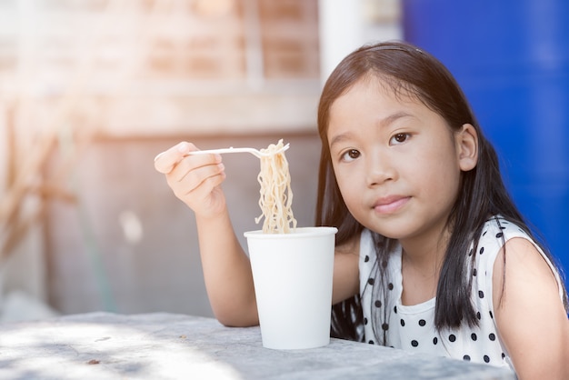 かわいいアジアの子供の女の子インスタント麺カップ、ファストフードコンセプトを食べる