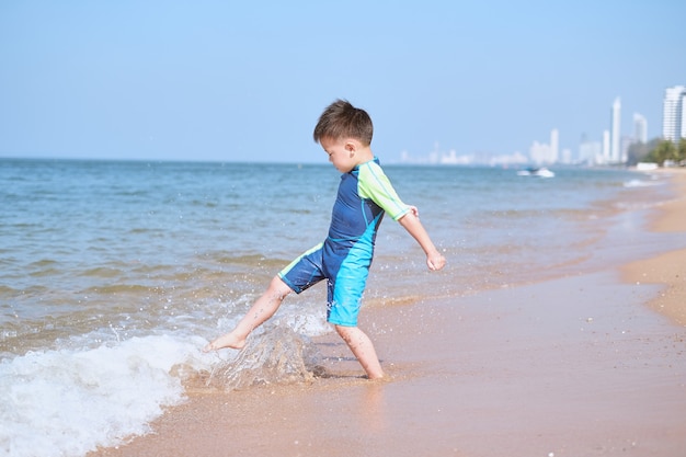 Cute Asian kid kicks the sea wave on the sandy beach