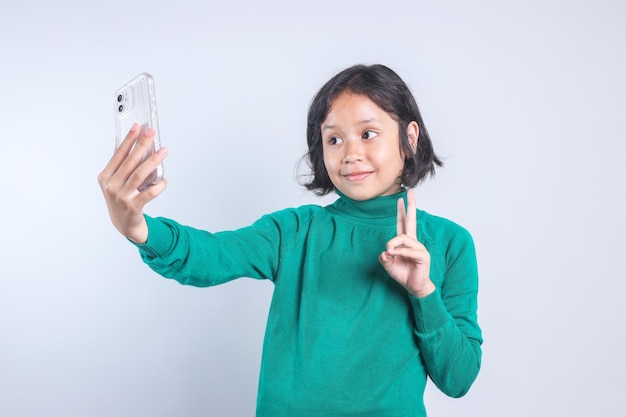 Cute Asian kid taking a selfie to send it to friends and followers or post it on her social media