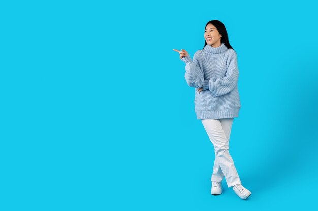 Cute asian lady in warm outwear pointing at copy space