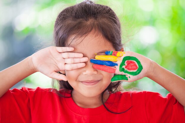 Ragazza asiatica sveglia del piccolo bambino con le mani dipinte che sorride con il divertimento e la felicità