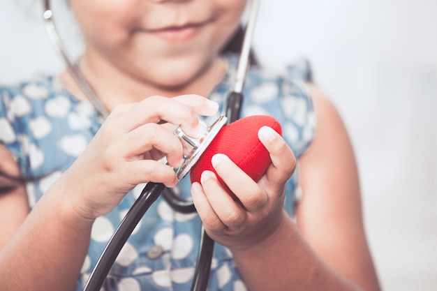 Симпатичные Азии маленькая девочка с стетоскоп, играя врач, чтобы слушать красное сердце в руке
