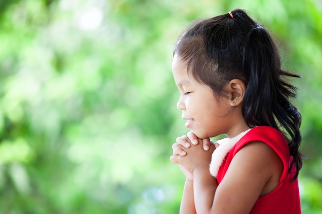 Cute asian little girl in christmas dress closed her eyes and folded her hand in prayer