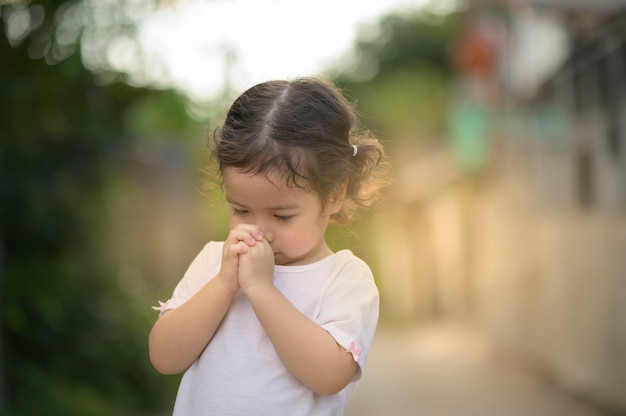 かわいいアジアの女の子は目を閉じ、朝に祈っています。小さなアジアの女の子の手祈り、手を組んで信仰、霊性および宗教のための祈りの概念。