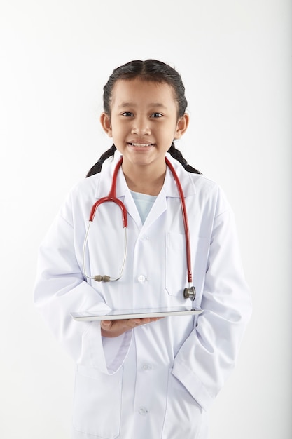 Cute Asian little girl in doctor costume with stethoscope and tablet smiling