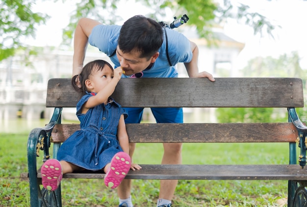 かわいいアジアの少女は、緑の公共公園の父親のためにクッキーを与える