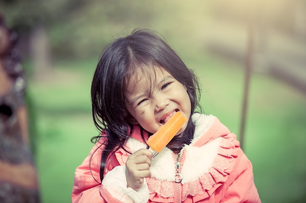 Cute asian little girl is eating ice-cream in the park in vintage color filter