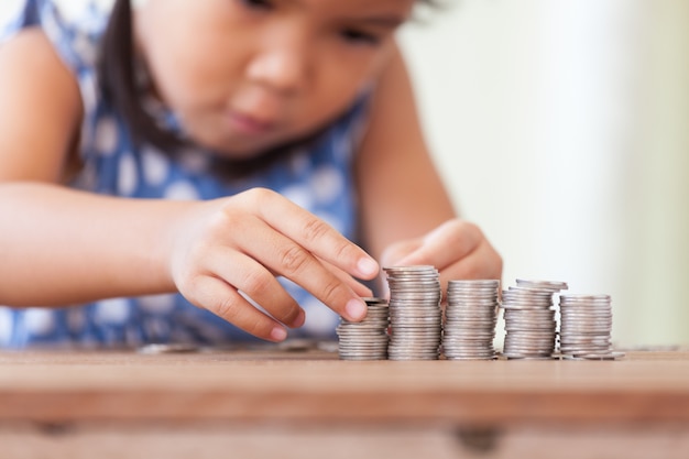 Cute asian little girl making stacks of coins. 