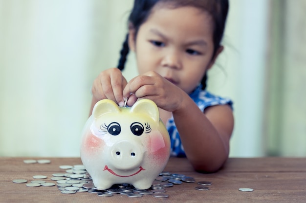 彼女のpiggybankのお金を節約しているかわいいアジアの少女