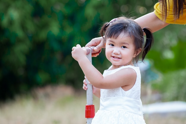 Милая азиатская маленькая девочка усмехаясь и играя в парке с потехой и счастьем