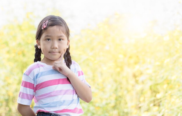 黄色い花の背景に考えているかわいいアジアの少女