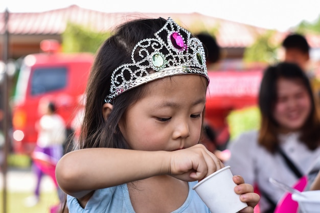 Bambina asiatica sveglia che usando cucchiaio che cerca qualcosa nella tazza.