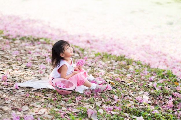かわいいアジアの少女がピンクのドレスを着て、ピンクの花の公園に座って