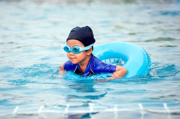 Cute asian little girl with swim ring is having fun in swimming pool