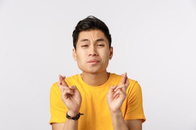 Милый азиатский мужчина в желтой футболке скрещивает пальцы на удачу