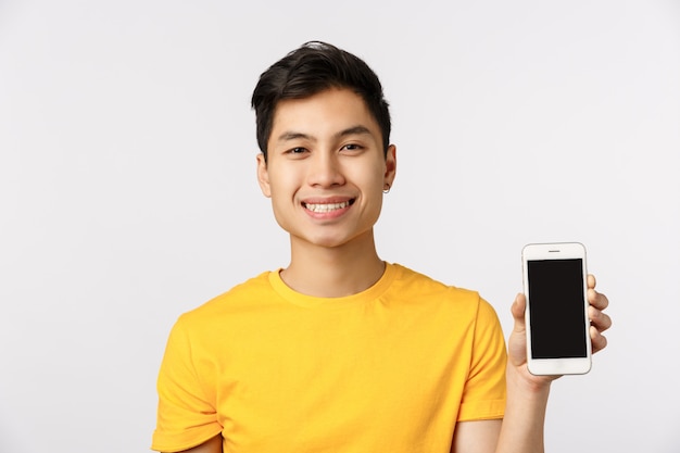 Cute asian man in yellow t-shirt showing smartphone