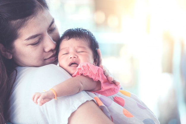 Cute asian newborn baby girl sleeping on mother's shoulder.