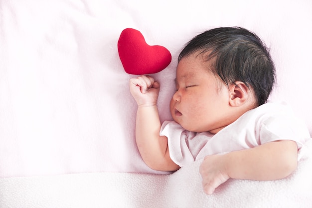 かわいいアジアの新生児の赤ちゃん少女赤い心で寝る