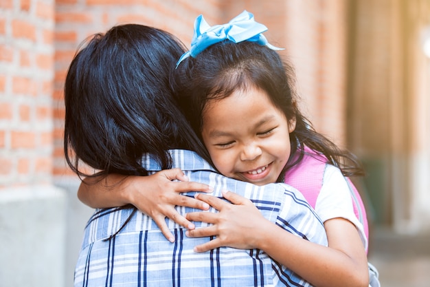 Cute asian pupil girl with backpack hugging her mother with happiness after back from school