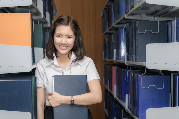 cute asian student holding book in library university, education concept