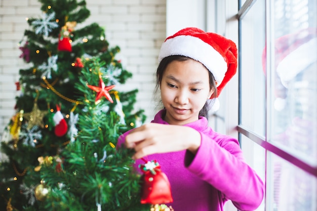 かわいいアジアのティーンエイジャーの女の子がクリスマスフェスティバルで祝うためのクリスマスツリーを飾る