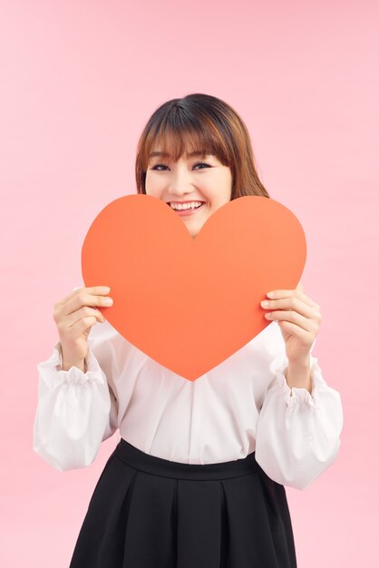 Photo cute asian woman holding red heart isolated on pink