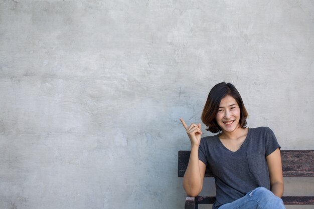 귀여운 아시아 여자는 회색 배경에 당신에게 뭔가를 보여줍니다.