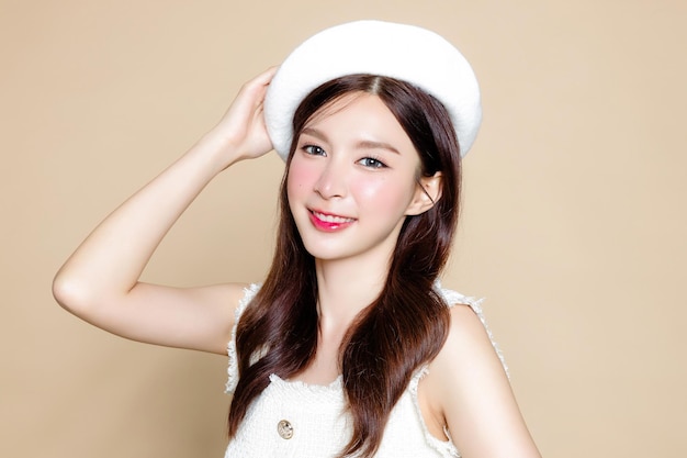 Cute asian woman with perfect clear fresh skin pretty girl\
model wearing white beret and natural makeup on beige background\
cosmetology beauty and spa wellness plastic surgery