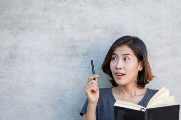 귀여운 아시아 여성은 회색 배경에 그녀의 책으로 무언가를 생각하고 있습니다