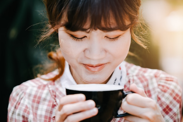 写真 かわいいアジアの女性は、コーヒーカップを笑顔で楽しむために飲むのは、