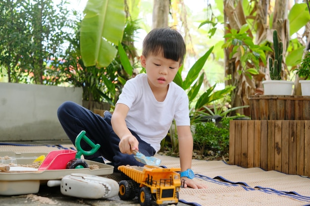 Cute Asian young kindergarten boy playing with sand and toy construction machinery alone at home