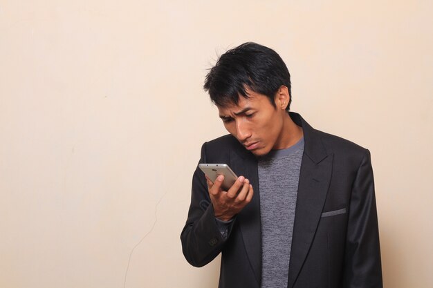 Cute Asian young man with curious checking his smartphone, wearing a suit with a sweater i