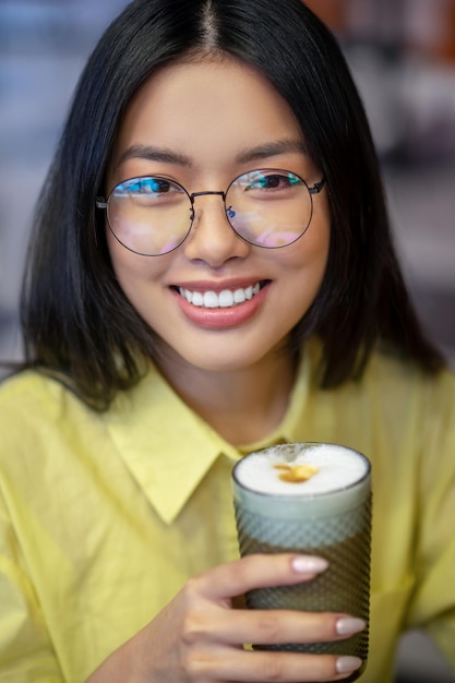 Cute asian young woman in eyeglasses at the laptop having coffee