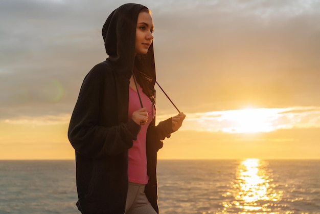 かわいい運動の女の子は、海のそばの夕方の太陽の光線で実行され、体重を減らしたい