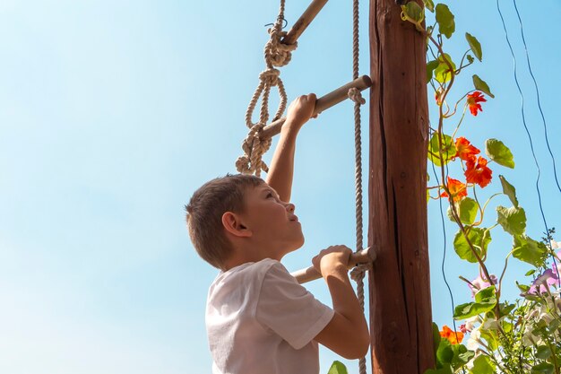 Cute athletic little boy child climbing on rope ladder high up.\
amusement park for kids. outdoor activities and games for children.\
way up concept