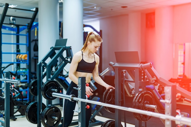 Cute athletic woman doing exercises with dumbbells. Fitness muscular body on modern gym background. Fitness concept.