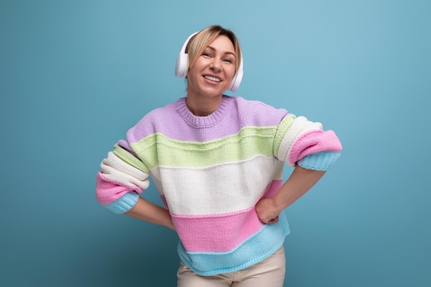 Cute attractive blond woman in a striped sweater in big wireless headphones enjoys a podcast on a